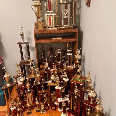 Sale Photo Thumbnail #116: Large collection of vintage sports trophies, primarily featuring golf and baseball figures with gold-toned finishes and wooden bases.
