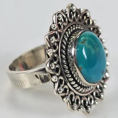 Vintage sterling silver ring featuring a large oval turquoise cabochon set in an ornate, scalloped filigree border with rope detailing.