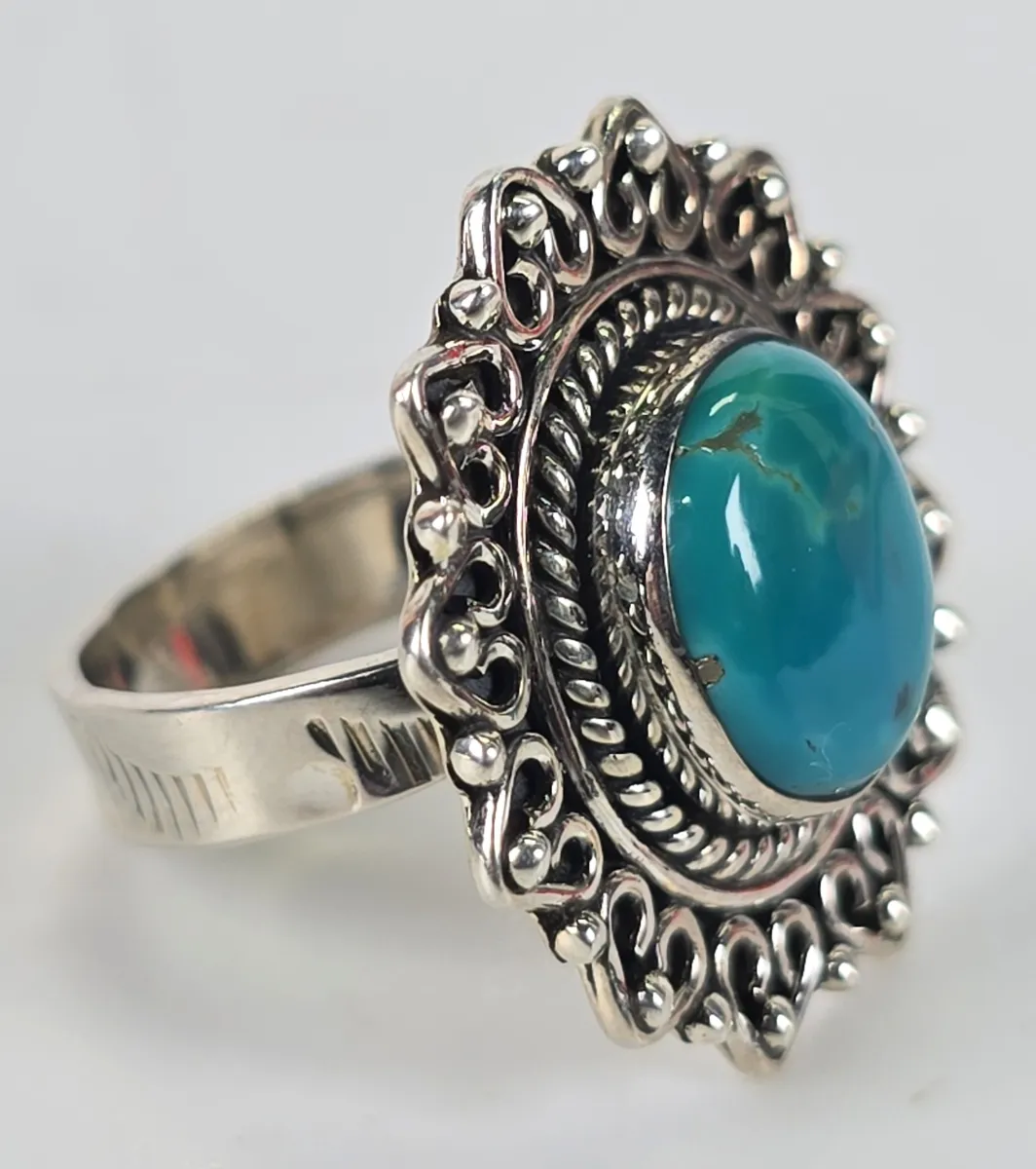 Vintage sterling silver ring featuring a large oval turquoise cabochon set in an ornate, scalloped filigree border with rope detailing.