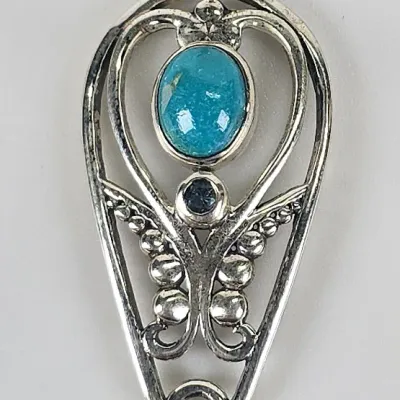 Sterling silver pendant featuring an oval turquoise cabochon, a small round dark blue gemstone, and a dangling teardrop-cut light blue...