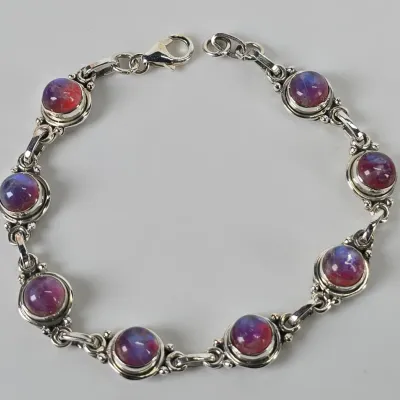 Sterling silver link bracelet featuring eight bezel-set, round cabochons with iridescent purple and red hues, secured with a lobster claw...