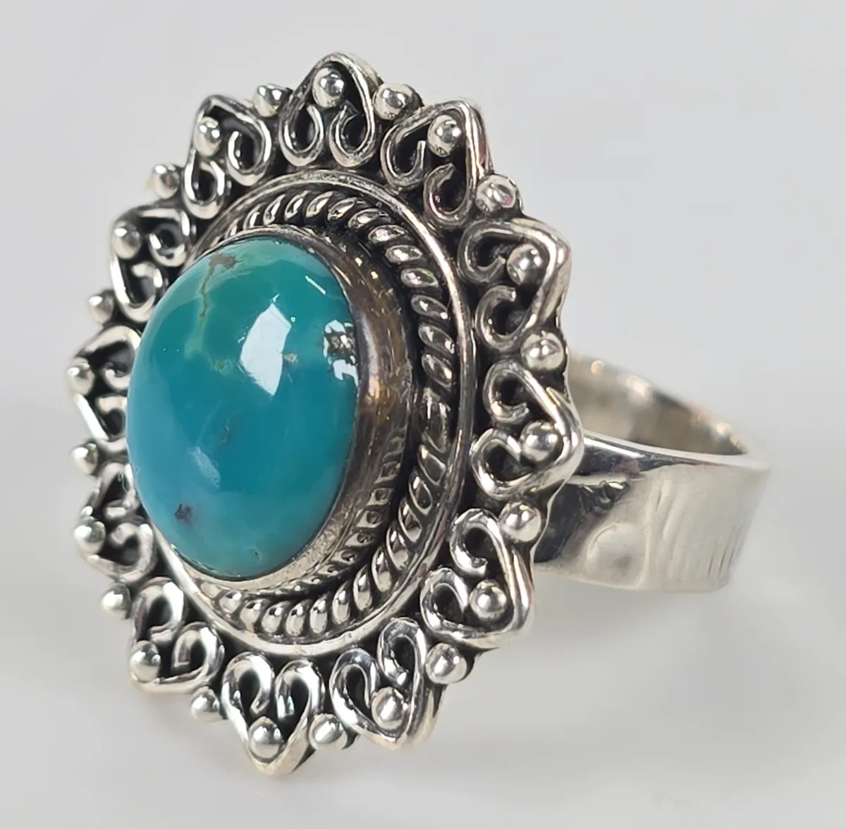 Sterling silver statement ring featuring an oval turquoise cabochon set in an ornate, scalloped filigree border with rope detailing.