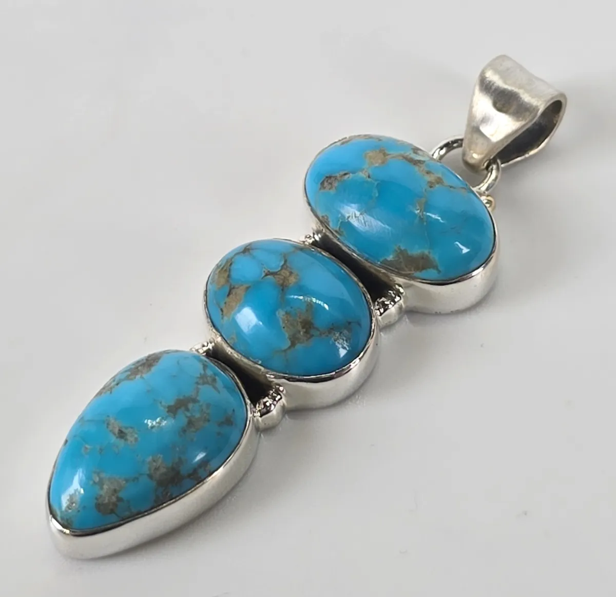 Southwestern-style sterling silver pendant featuring three graduated, bezel-set turquoise cabochons with natural matrix.
