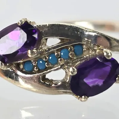 Sterling silver bypass ring featuring two oval-cut purple amethysts accented by a row of small round turquoise stones.