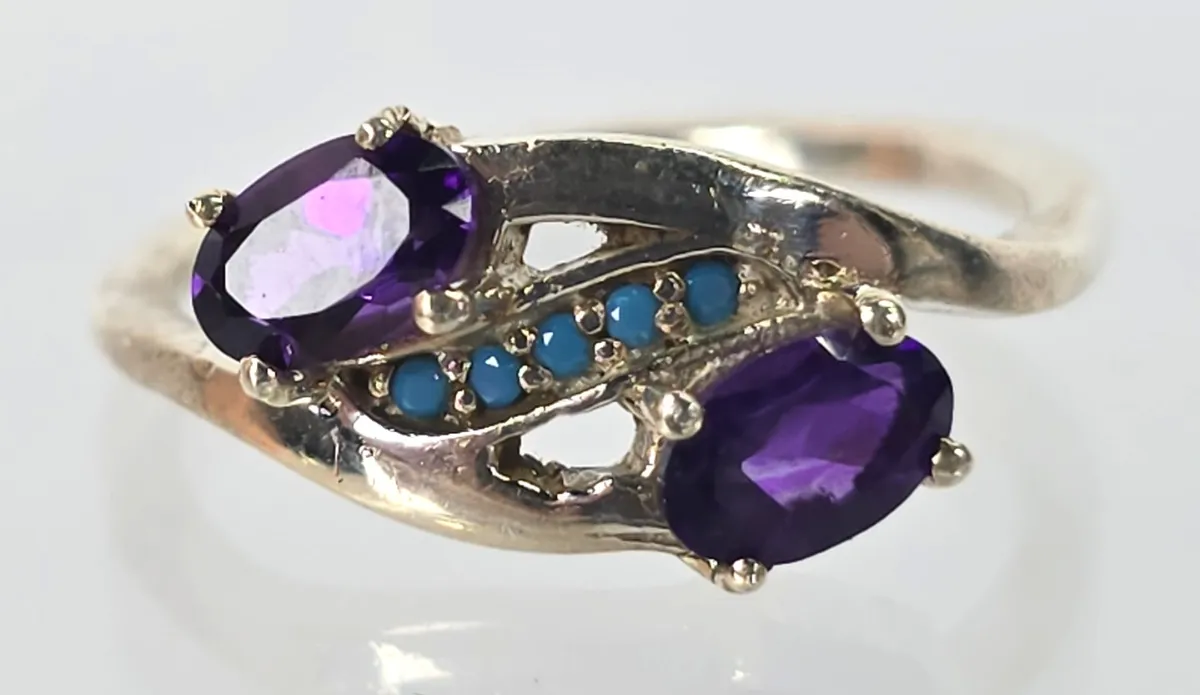 Sterling silver bypass ring featuring two oval-cut purple amethysts accented by a row of small round turquoise stones.