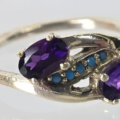 Sterling silver bypass ring featuring two oval-cut purple amethyst gemstones accented by a diagonal row of small round turquoise stones.