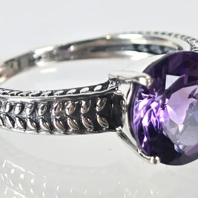 Sterling silver ring featuring a round-cut purple amethyst gemstone in a four-prong setting, accented by a textured, wheat-patterned band...