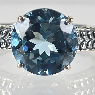 Sterling silver ring featuring a large, round-cut London blue topaz in a four-prong setting, accented by a textured, openwork band.