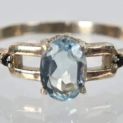 Gold-tone ring featuring an oval-cut light blue gemstone, possibly aquamarine or blue topaz, flanked by openwork shoulders and small...
