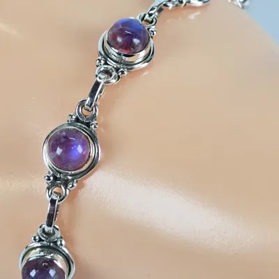 Sterling silver link bracelet featuring bezel-set, round cabochon amethyst stones with delicate beaded metalwork details.