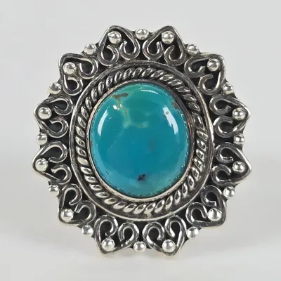 Vintage sterling silver ring featuring a large, oval turquoise cabochon set in an ornate, scalloped border with rope and bead detailing.