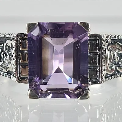 Vintage-style sterling silver ring featuring an emerald-cut purple amethyst gemstone set in an ornate, filigree-detailed band.