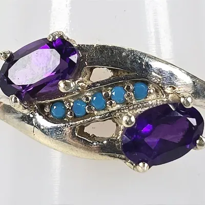 Sterling silver bypass ring featuring two oval-cut amethyst gemstones accented by a row of small turquoise cabochons.