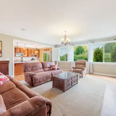 Spacious living room featuring a brown leather reclining sofa and loveseat, a dark wood coffee table with drawers, and a patterned...