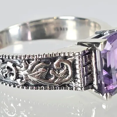 Sterling silver ring featuring an emerald-cut purple amethyst gemstone set in a band with ornate, oxidized filigree detailing.