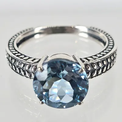 Sterling silver ring featuring a round-cut blue topaz gemstone set in a four-prong mount, accented by a textured, wheat-patterned band.