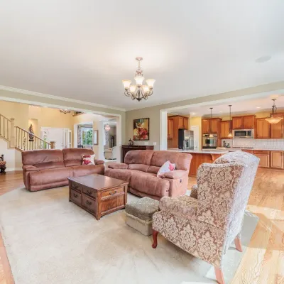 Spacious open-concept living room featuring two brown leather reclining sofas, a wooden coffee table, a patterned armchair with a...