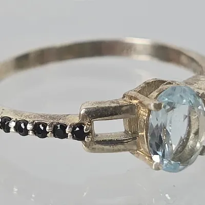 Sterling silver ring featuring an oval-cut light blue topaz or aquamarine center stone, accented by small black stones along the shoulders.