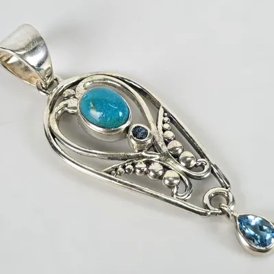 Sterling silver teardrop pendant featuring a bezel-set turquoise cabochon, a small round blue gemstone, and a dangling pear-cut blue...