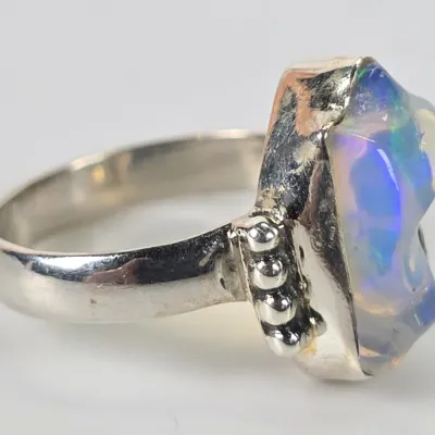 Sterling silver ring featuring a raw, freeform opal with vibrant blue and green play-of-color, accented by beaded detailing on the...
