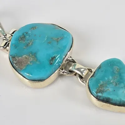 Sterling silver pendant featuring two freeform turquoise stones in bezel settings, connected by a hinged link.