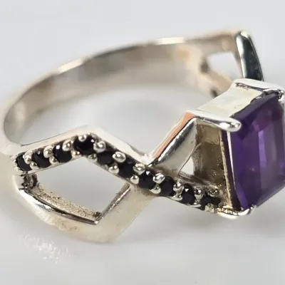 Sterling silver ring featuring an emerald-cut purple amethyst center stone flanked by black spinel accents on a split-shank band.