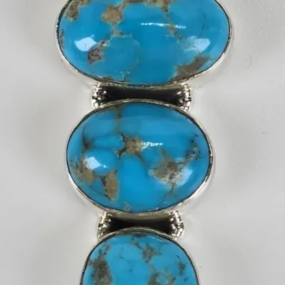 Southwestern-style sterling silver pendant featuring three tiered, bezel-set turquoise cabochons with natural matrix patterning.