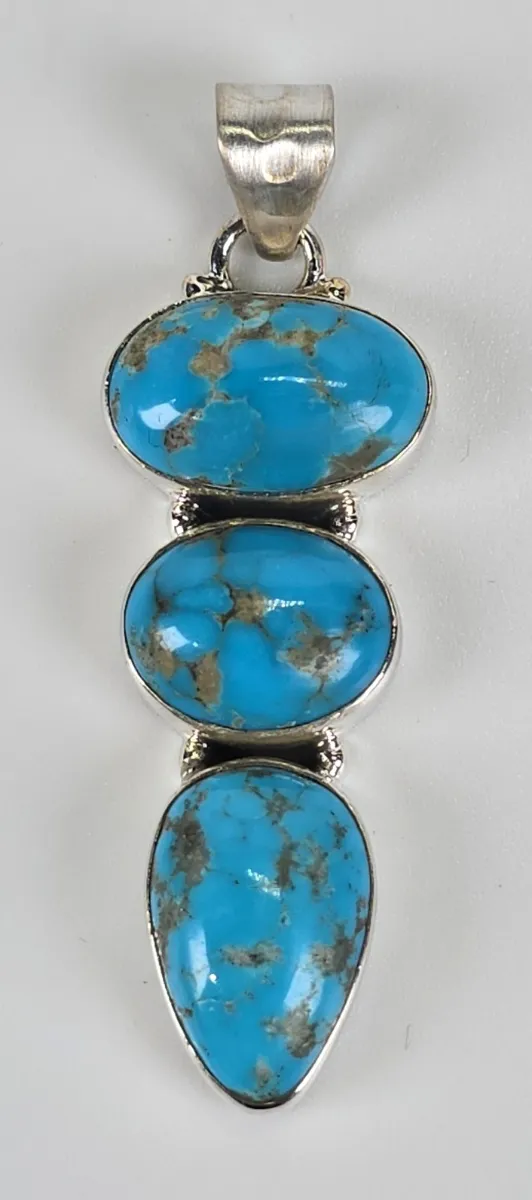 Southwestern-style sterling silver pendant featuring three tiered, bezel-set turquoise cabochons with natural matrix patterning.