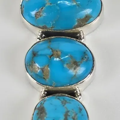 Sterling silver pendant featuring three bezel-set turquoise cabochons with natural matrix, arranged in a vertical drop design.