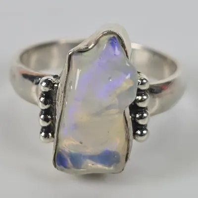 Sterling silver ring featuring a freeform raw opal with blue and purple play-of-color, accented by beaded silver details on the shoulders.
