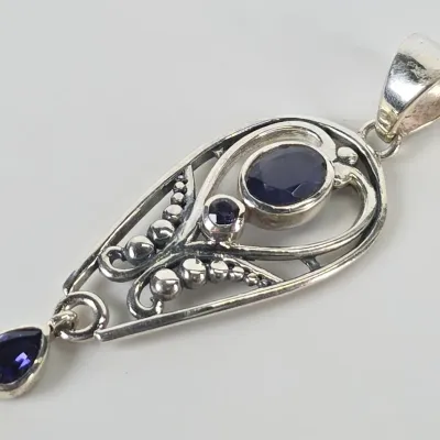 Sterling silver teardrop pendant featuring intricate filigree work, beaded accents, and three bezel-set dark blue gemstones, including a...