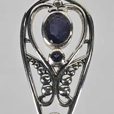 Sterling silver pendant featuring three bezel-set purple gemstones, possibly iolite or amethyst, in an openwork filigree design with a...
