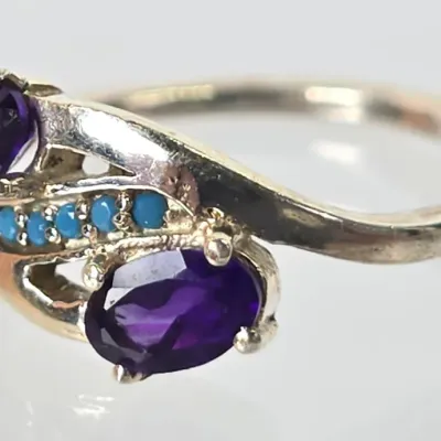 Sterling silver bypass ring featuring two oval-cut purple amethyst gemstones accented by a row of small turquoise cabochons.