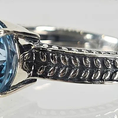 Sterling silver ring featuring a round-cut blue topaz gemstone in a four-prong setting, accented by a textured, oxidized wheat-pattern band.
