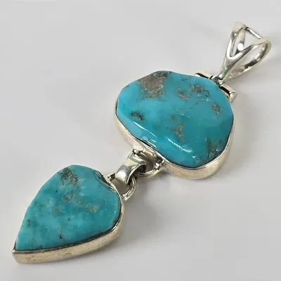 Southwestern-style sterling silver pendant featuring two freeform turquoise stones with natural matrix, connected by a silver link.