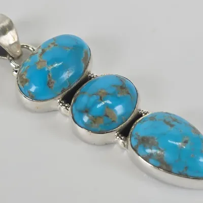 Southwestern-style sterling silver pendant featuring three graduated, bezel-set turquoise cabochons with natural matrix.