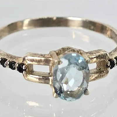 Sterling silver ring featuring an oval-cut light blue topaz center stone flanked by small black accent stones on the shoulders.