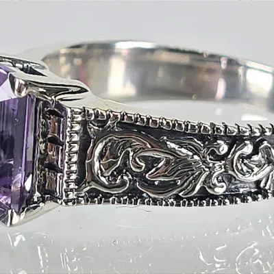 Sterling silver ring featuring an emerald-cut amethyst stone set in a band with ornate, oxidized scrollwork detailing.