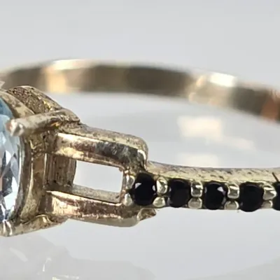 Sterling silver ring featuring an oval-cut light blue topaz center stone flanked by small black accent stones on a split-shoulder band.