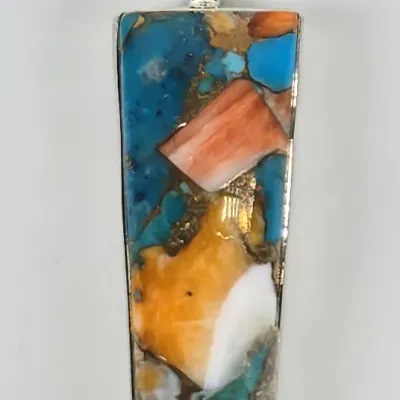 Elongated trapezoidal pendant featuring a mosaic of turquoise, spiny oyster shell, and other stones set in sterling silver.