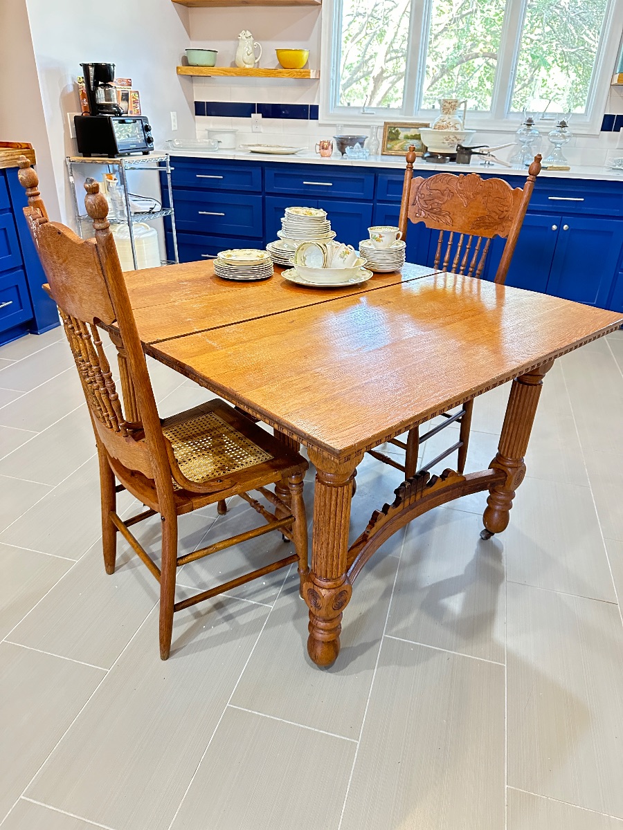 Antique oak dining table with thick fluted legs and a decorative under-stretcher, paired with two pressed-back oak chairs featuring cane...