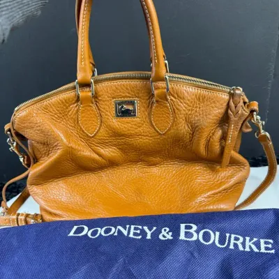Tan pebbled leather satchel from Dooney & Bourke, featuring dual top handles, a metal logo plaque, a