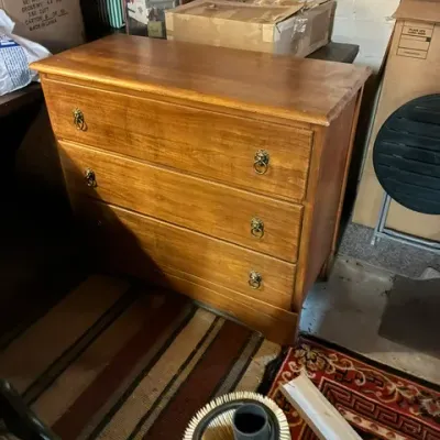 Vintage three-drawer wooden chest of drawers with brass lion head ring pulls, showing some wear on the top surface.