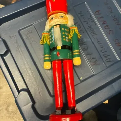 Vintage wooden toy soldier nutcracker featuring a green jacket with gold fringe epaulets, red pants, and a tall red hat.