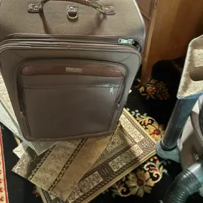 Vintage brown soft-sided rolling suitcase with faux-alligator trim and a braided handle, resting on small patterned rugs.