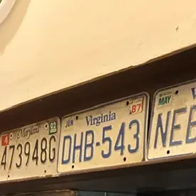 Collection of vintage Virginia and Maryland license plates from the late 1980s and early 2000s, displayed on a wooden shelf.
