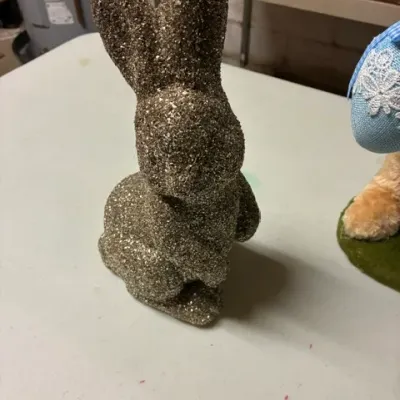 Decorative Easter bunny figurine covered in gold glitter, shown sitting on a white table.