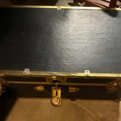 Vintage black steamer trunk with brass hardware, showing some wear on the metal trim.