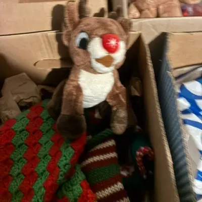 Plush Rudolph the Red-Nosed Reindeer toy sitting in a cardboard box alongside crocheted Christmas stockings.