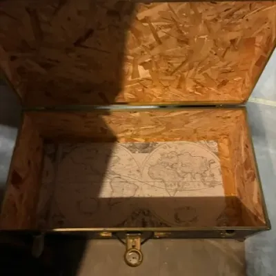 Open storage trunk featuring an oriented strand board interior and a vintage-style world map lining the bottom.